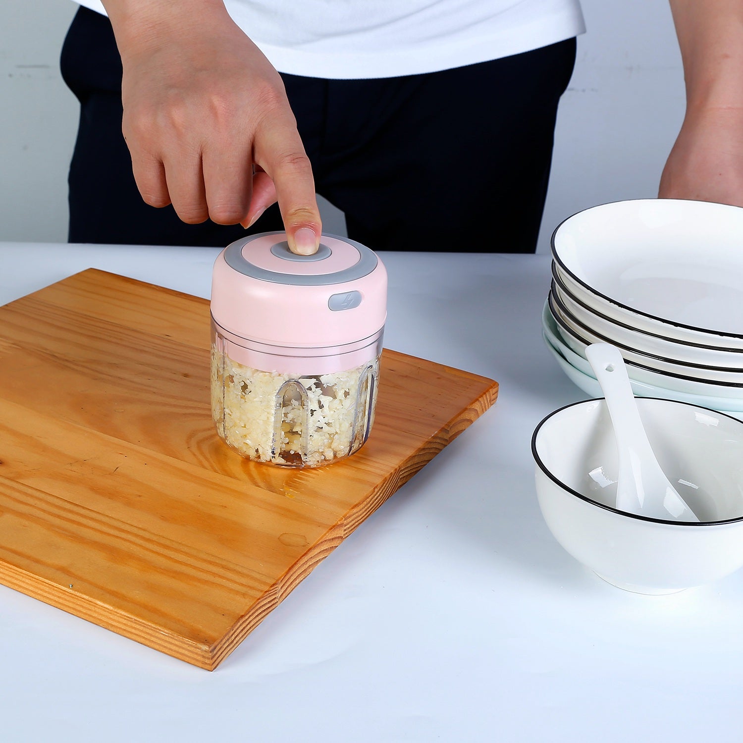 Handheld food chopper on a wooden cutting board with bowls and spoons in the background